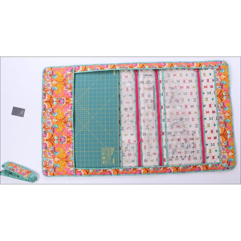 K&ouml;nnte beinhalten: Eine N&auml;h- und Quilt-Projektmatte mit einer t&uuml;rkisfarbenen Schneidefl&auml;che, einem floral gemusterten Rand und mehreren Taschen. Die Matte enth&auml;lt einen passenden Griff. Der Rand weist orangefarbene, rosa und blaue Blumenmuster auf.