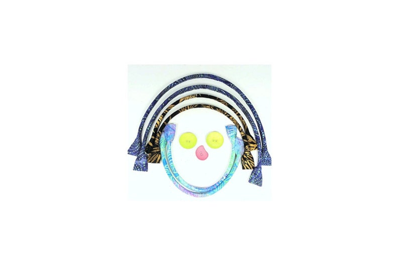 May include: A whimsical arrangement of fabric bag handles in various patterns, including blue batik and zebra print, arranged in an arc. Two yellow buttons and a pink button form a face.