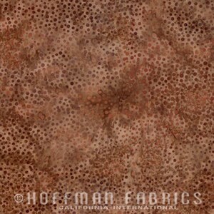 May include: Close-up of a brown and tan fabric with a mottled pattern of small, irregular dots. The fabric has a textured appearance, with variations in color and density. The text "HOFFMAN FABRICS CALIFORNIA INTERNATIONAL" is printed at the bottom.