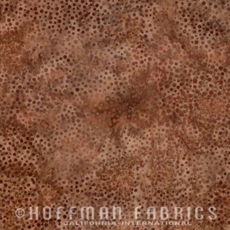 May include: Close-up of a brown and tan fabric with a mottled pattern of small, irregular dots. The fabric has a textured appearance, with variations in color and density. The text "HOFFMAN FABRICS CALIFORNIA INTERNATIONAL" is printed at the bottom.