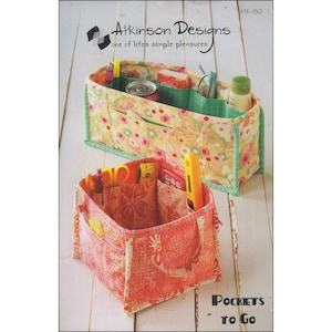 May include: Two fabric storage organizers with pockets, filled with various items. The top organizer is yellow with a floral pattern, green trim, and contains pens, a can, and a bottle. The bottom organizer is pink with a floral pattern and has handles. Text reads "Pockets to Go."