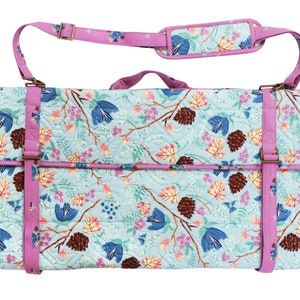 K&ouml;nnte beinhalten: Eine rechteckige, gesteppte Tasche mit floralem Muster in Blau, Rosa und Braun. Sie hat einen lila Besatz und Tr&auml;ger, einschlie&szlig;lich eines gepolsterten Schultergurts. Die Tasche wird mit einer Klappe und verstellbaren Riemen mit Metallschnallen verschlossen. Ca. 60 cm lang.