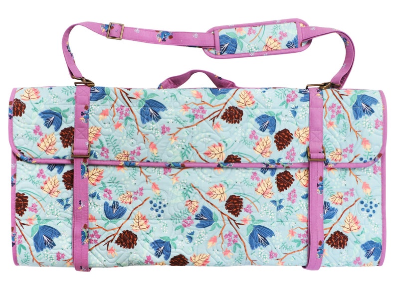 K&ouml;nnte beinhalten: Eine rechteckige, gesteppte Tasche mit floralem Muster in Blau, Rosa und Braun. Sie hat einen lila Besatz und Tr&auml;ger, einschlie&szlig;lich eines gepolsterten Schultergurts. Die Tasche wird mit einer Klappe und verstellbaren Riemen mit Metallschnallen verschlossen. Ca. 60 cm lang.
