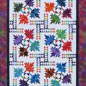 May include: A colorful quilt featuring a repeating pattern of stylized maple leaves in shades of red, orange, blue, green, and purple. The leaves are set against a white background with a border of triangles and a patterned edge.