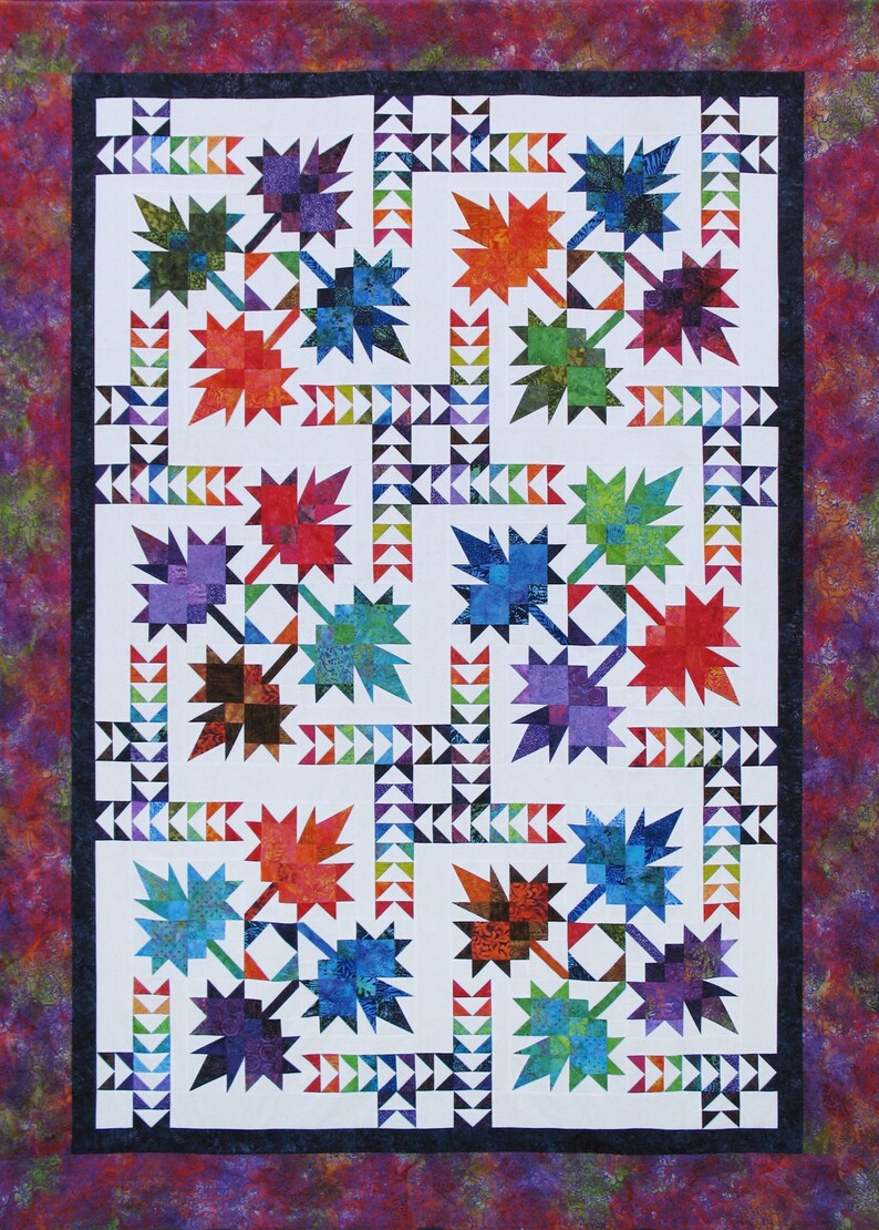 May include: A colorful quilt featuring a repeating pattern of stylized maple leaves in shades of red, orange, blue, green, and purple. The leaves are set against a white background with a border of triangles and a patterned edge.