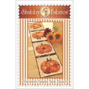 May include: A patchwork pumpkin table runner with four pumpkin designs. The pumpkins are made of orange and brown fabric squares. The runner is on a light beige background with a brown border. The text "Shabby Fabrics" is at the top.