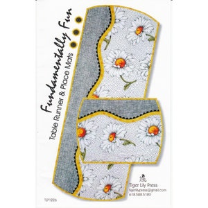 May include: A table runner and place mat set with a daisy floral pattern. The set includes a long, rectangular table runner and two place mats. The table runner and place mats have a gray border with a yellow trim and black scalloped edge. The text "Fundamentally Fun Table Runner & Place Mats" is printed on the left side.