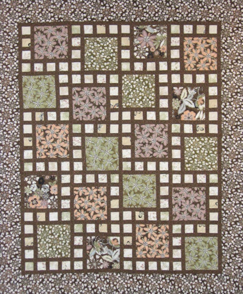 May include: A handmade quilt with a grid pattern. The quilt features squares of floral fabric in shades of green, peach, and brown, set against a brown grid. The border is a floral pattern on a brown background. A cozy, decorative textile.
