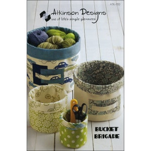 May include: A collection of fabric storage buckets in various sizes and patterns. The largest bucket features a blue car print, while others display floral, polka dot, and bicycle designs. The text "BUCKET BRIGADE" is visible.
