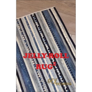 May include: A rectangular rug with vertical stripes in shades of blue, gray, and white. The stripes feature various patterns, including dots, geometric shapes, and solid colors. The text "JELLY ROLL RUG" is displayed in red across the center.