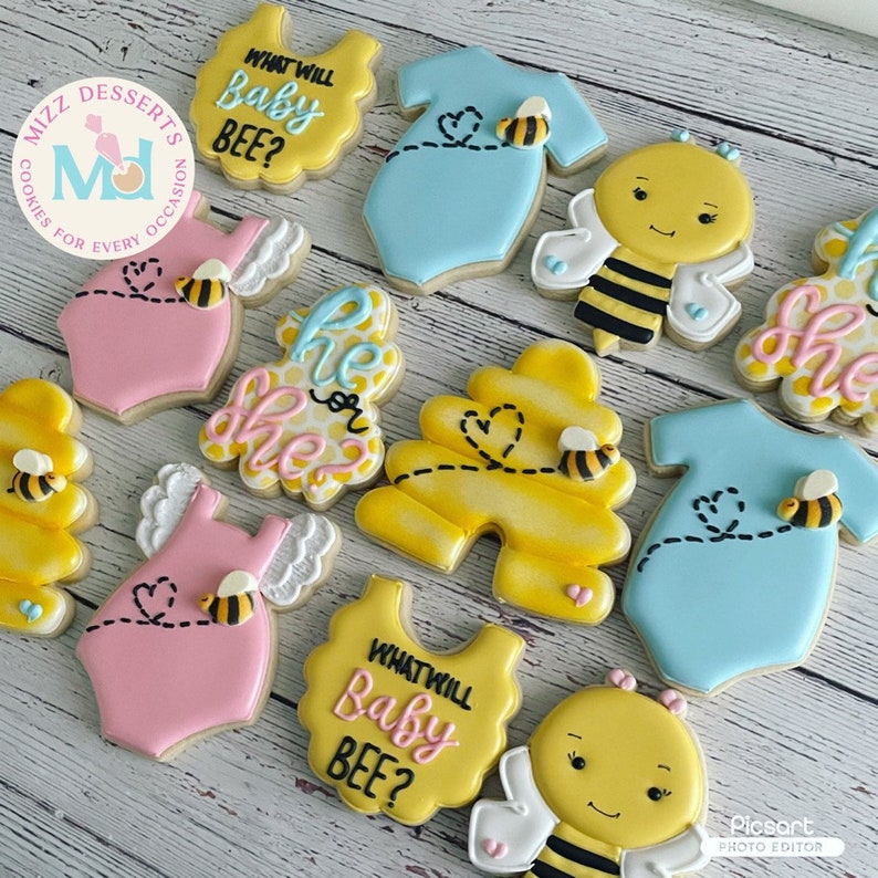 Pode incluir: Um conjunto de nove biscoitos de a&ccedil;&uacute;car decorados com um tema de abelhas. Os biscoitos s&atilde;o decorados com glac&ecirc; amarelo, azul, rosa e branco. Os biscoitos apresentam o texto "What will Baby Bee?" e "He or She?"
