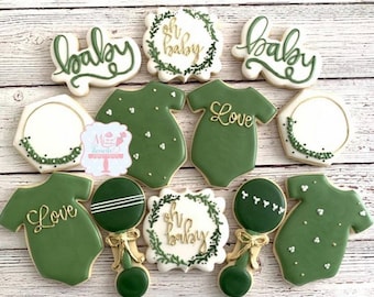 Puede incluir: Un conjunto de 10 galletas verdes y blancas para baby shower decoradas con letras doradas. Las galletas presentan varios diseños, incluyendo bodies, coronas y sonajeros. Las galletas están decoradas con las palabras "Oh Baby", "Love" y "Baby".
