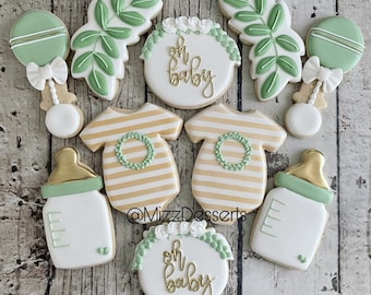 Puede incluir: Un conjunto de nueve galletas de azúcar decoradas con un tema de baby shower. Las galletas están decoradas con hojas verdes, rayas doradas y las palabras "Oh Baby".
