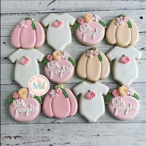 May include: A set of 10 decorated sugar cookies featuring a pumpkin and onesie design. The cookies are decorated with pink, white, and orange icing and have the words "little pumpkin" written on them.