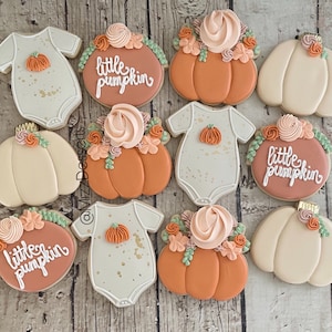 May include: Nine decorated sugar cookies with fall themes. The cookies are decorated with orange, brown, and white frosting. Some cookies have the words "little pumpkin" written on them. Others are decorated with flowers and leaves.