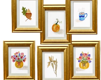 May include: Six framed watercolour paintings in gold frames. The paintings depict an acorn, a pumpkin, a mug of hot chocolate, a vase of flowers, an iris, and a vase of flowers. The paintings are on a white background.
