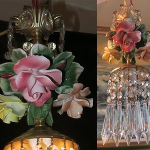 May include: A vintage chandelier with a floral design. The chandelier features a cluster of porcelain roses in shades of pink, white, and yellow, with green leaves. The chandelier is adorned with crystal prisms that hang from the bottom.