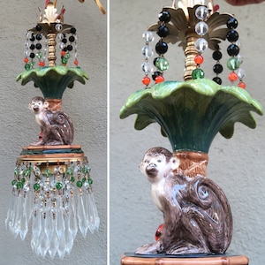 May include: A vintage chandelier featuring a ceramic monkey figure. The fixture has a green leaf-shaped shade, crystal accents, and beaded strands in various colors. The chandelier has a gold-colored metal frame.