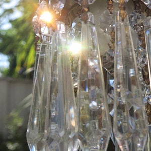 May include: Close-up of a crystal chandelier with multiple strands of faceted crystal prisms hanging from a brass fixture. The crystals are catching the sunlight, creating a sparkling effect.