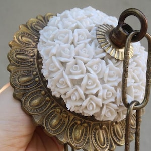 May include: A brass ceiling fixture with a white porcelain rose design. The fixture has a chain and a hook for hanging.