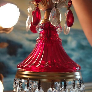 May include: A red glass chandelier with crystal drops. The chandelier has a gold-colored metal base and a red glass shade with a fluted design.