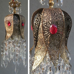 May include: A gold metal chandelier with a floral design and crystal accents. The chandelier has red glass jewels and a delicate, intricate pattern.