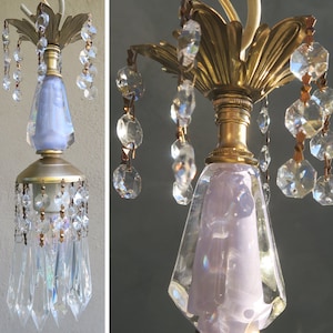 May include: A vintage chandelier with a brass-colored base and a light purple glass center. Clear crystal teardrops and faceted beads hang from the fixture, adding sparkle. The chandelier has a classic, elegant design.