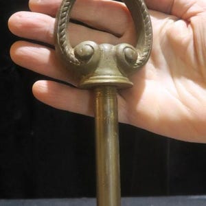 May include: Antique brass drawer pull with a decorative ring handle. The handle features a rope-like texture and ornate detailing. The pull has a long, threaded post for secure attachment to furniture. A vintage hardware piece.