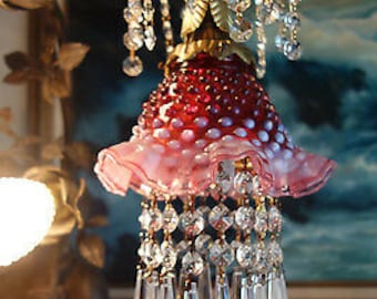 May include: A vintage chandelier with a red and white dotted glass shade and a pink ruffled edge. The chandelier features crystal accents and a gold-colored metal frame. The design is ornate and decorative.