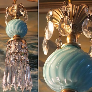 Puede incluir: Una lámpara de araña vintage con una pantalla de vidrio azul y detalles de cristal. La lámpara de araña tiene un marco de metal dorado y está adornada con una fila de gotas de cristal.