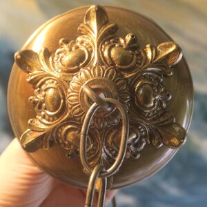 May include: A gold-toned metal ceiling fixture with an ornate design and a chain hanging from the center.