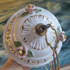May include: White porcelain ceiling light fixture with gold accents and floral details. The fixture has a round shape and features delicate pink roses and green leaves.