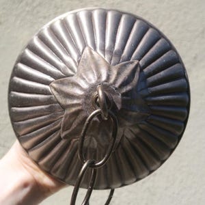 May include: A silver-toned, round ceiling light fixture with a star-shaped detail and a chain. The fixture has a ribbed design radiating from the star. The light fixture is made of metal.