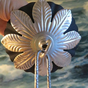 May include: A silver metal ceiling fixture with a decorative leaf design. The fixture has a black backing and a hook for hanging.