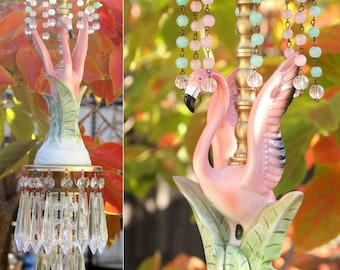 May include: A pink flamingo lamp with a gold base and crystal accents. The lamp features a pink flamingo with green leaves and a gold base with crystal beads hanging from it.