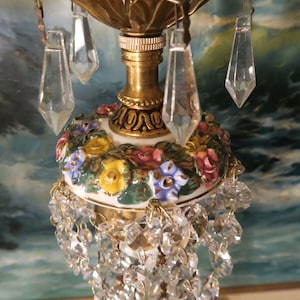 May include: A vintage lamp with a white porcelain base decorated with colorful flowers and a gold metal top with crystal accents.