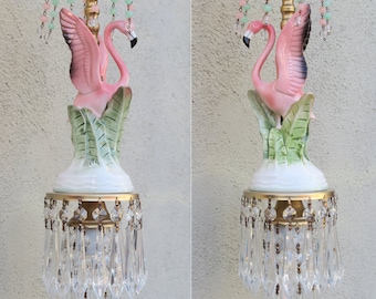Może przedstawiać: Lampa wisząca w kształcie różowego flaminga z kryształowymi kroplami i zielonymi koralikami. Flaming  siedzi na podstawie z zielonych liści. Lampa wisząca jest wykonana z ceramiki i metalu.