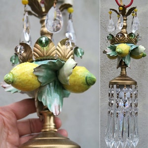 May include: A gold chandelier with a cluster of porcelain lemons and green leaves. The chandelier has a crystal teardrop design.