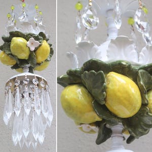 May include: A white ceramic chandelier with a cluster of yellow lemons and green leaves. The chandelier has a crystal teardrop design.