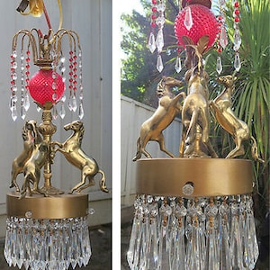 May include: A gold chandelier with three horse figures and a red glass shade. The chandelier is adorned with crystal prisms and beads.