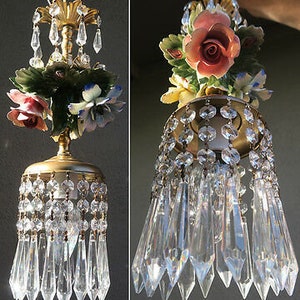 May include: A hanging light fixture featuring a gold-tone metal frame adorned with porcelain flowers, including pink roses and blue blossoms. The fixture is decorated with clear glass crystal beads and long, pointed crystal prisms hanging below.