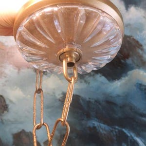 May include: A vintage-style ceiling light fixture with a clear, ribbed glass shade and a gold-colored metal frame. The fixture includes a gold chain for hanging. The design is reminiscent of classic lighting.