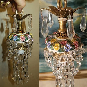 May include: A gold and white porcelain chandelier with floral details and crystal drops. The chandelier has a floral design with pink, yellow, and blue flowers. The crystal drops are clear and hang from the chandelier in a cascading pattern.