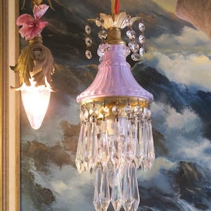 May include: A vintage-style chandelier with a pale pink glass shade and crystal drops. The chandelier is hanging from a ceiling and has a gold finish.