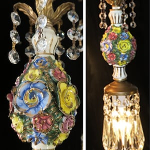 May include: A pair of ornate, white porcelain chandelier pendants with gold accents and crystal drops. The pendants are decorated with colorful flowers and leaves.
