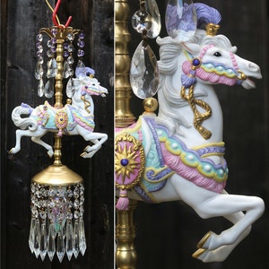 May include: A white porcelain carousel horse with pink, purple and blue accents. The horse is attached to a gold metal pole with crystal drops hanging from it.