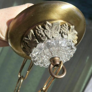 May include: Brass ceiling fixture with a decorative grapevine design and a clear glass shade. The fixture is attached to a chain.