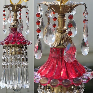 May include: A red glass chandelier with crystal drops and a brass frame. The chandelier has a red glass shade and a brass base.