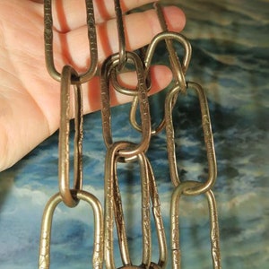 May include: A close-up of a gold chain with oval links. The links have a decorative pattern.