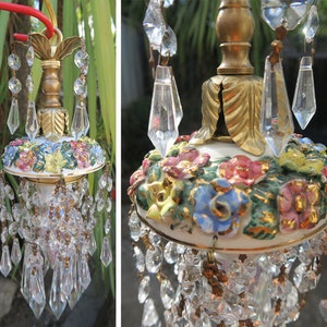 May include: A hanging light fixture featuring a central brass-toned metal stem with a leaf-shaped top. A white ceramic base is adorned with hand-painted, raised floral motifs in pink, blue, and yellow, accented by numerous clear glass crystals.
